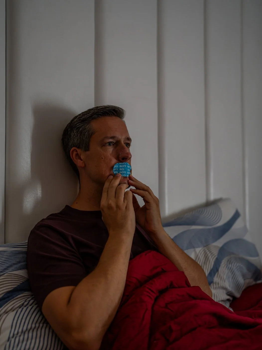 Muškarac u krevetu lepi Noro Mouth Tape preko usana